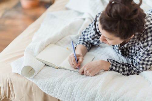 Woman writing on bed in journal