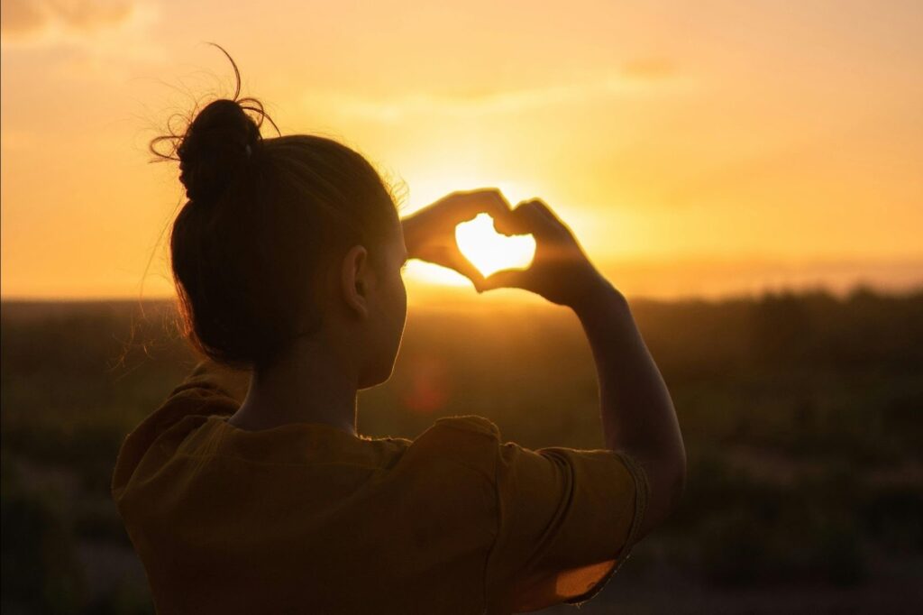 Woman looking towards the sun making a heart with her hands