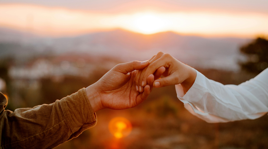 Two hands gently reaching for each other at sunset, a micro-connection and small gesture that builds trust in relationships