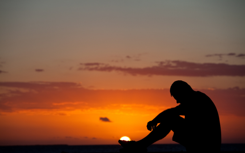 Person sitting alone at sunset reflecting on non-linear healing and therapy progress