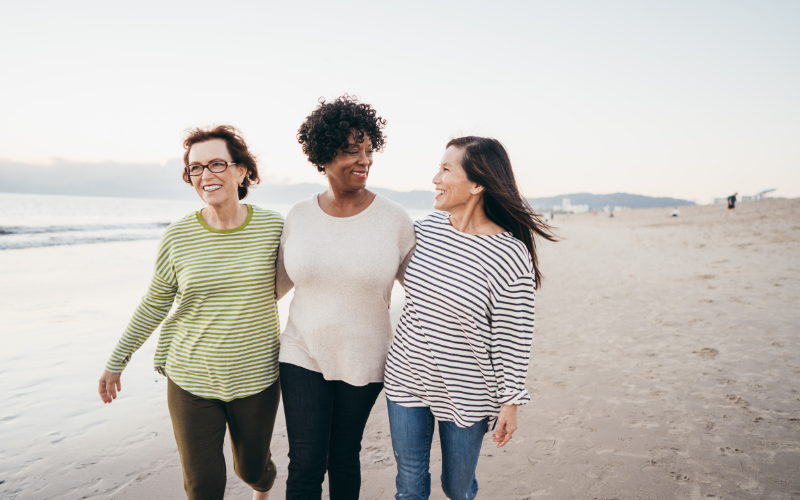 Three women walking together on beach representing support during non-linear healing journey
