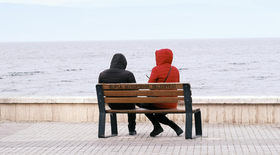 Two friends sitting together on a park bench, having an open and supportive conversation outdoors.