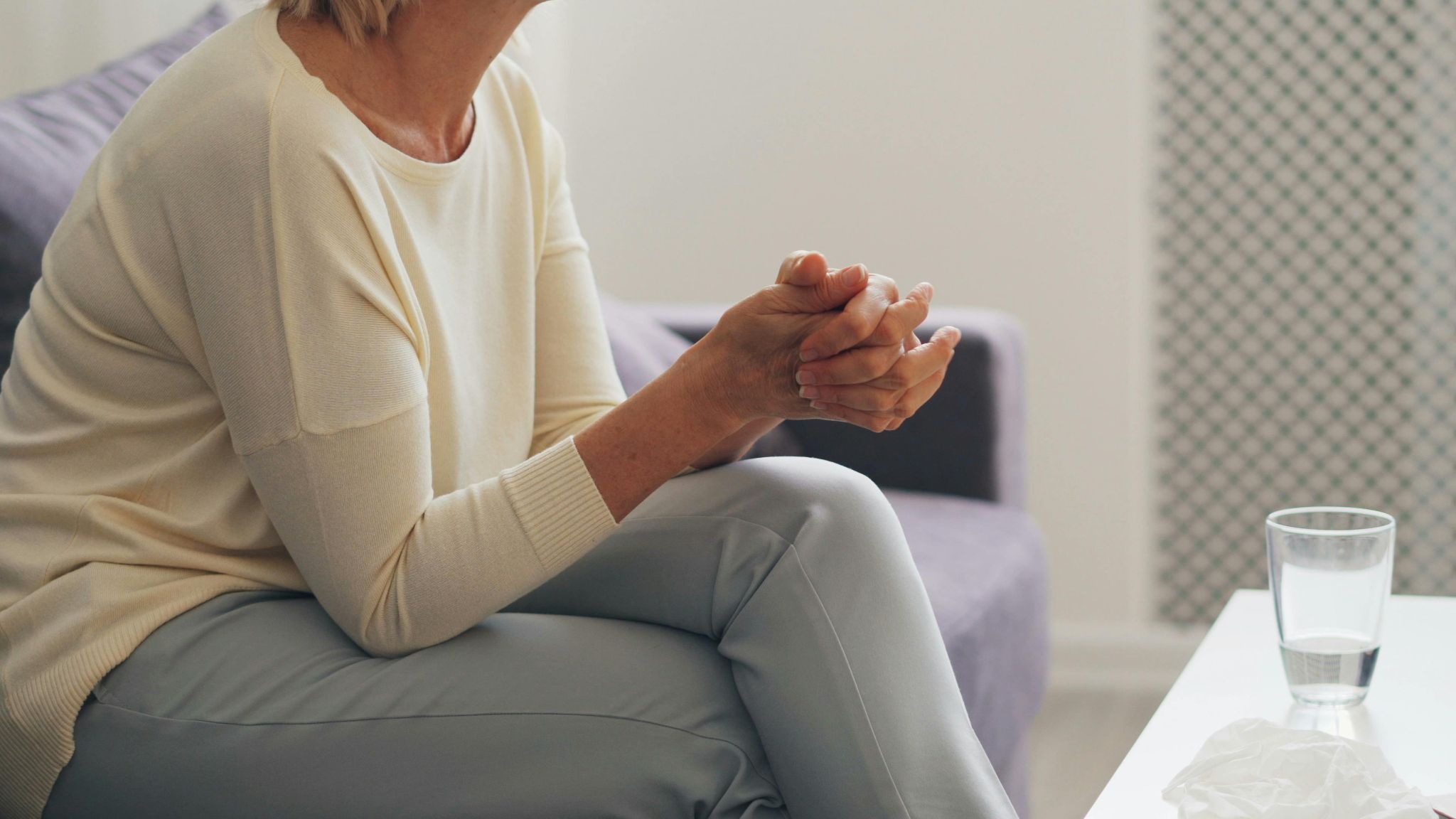A person with tightly clasped hands sitting near a box of tissues, illustrating the emotional moments of learning how to help someone with their mental health.
