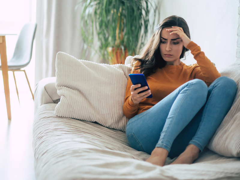 Women sitting on a couch scrolling through her phone.