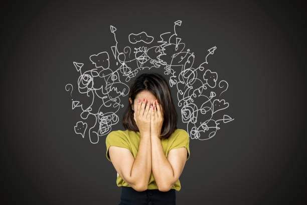 A woman in a green top covers her face with her hands in frustration. Above her head, a chaotic cloud of white, tangled scribbles is drawn against a dark grey background, representing severe stress, anxiety, or mental clutter.