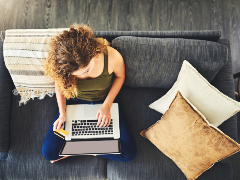 Woman sitting on coach with laptop on lap looking at screen.
