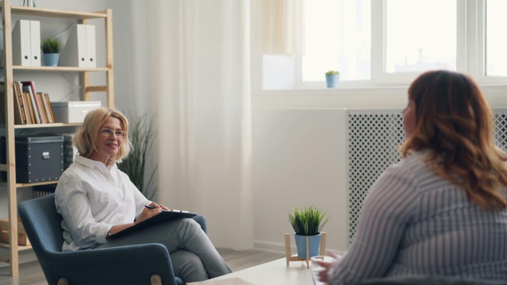 A therapist and client sitting across from each other in a bright, comfortable office, engaged in a calm and attentive conversation with soft natural light and minimal decor.
