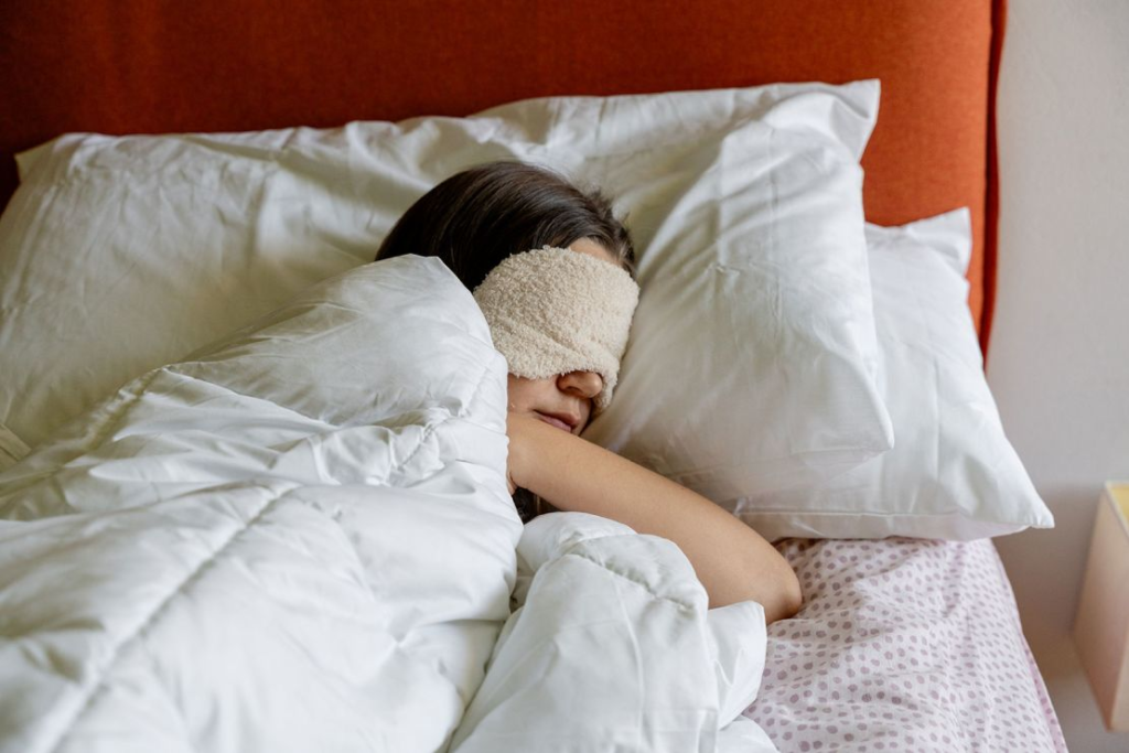 A tired woman resting in bed with a sleep mask on.
