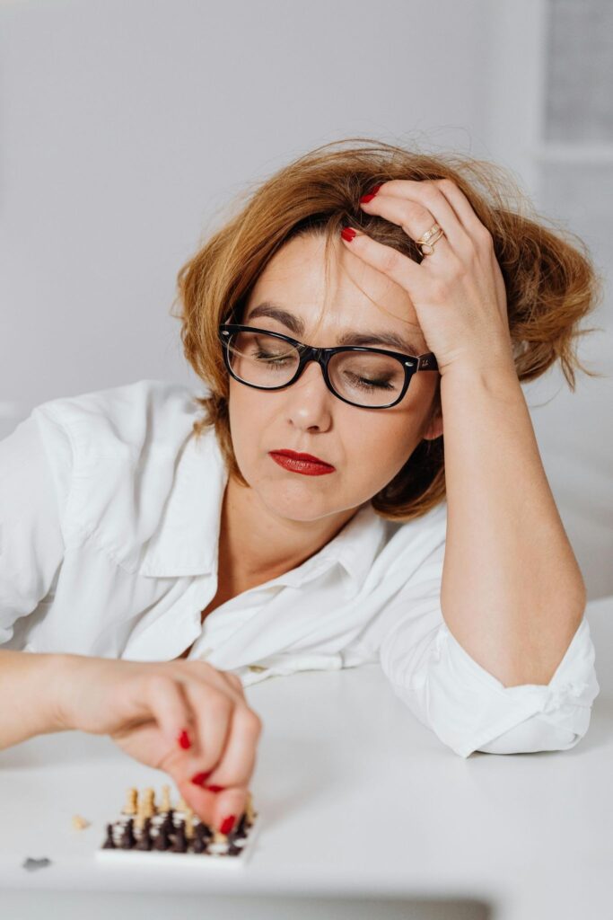 A woman with a disgruntled and sad expression playing a game on a miniature chess set.