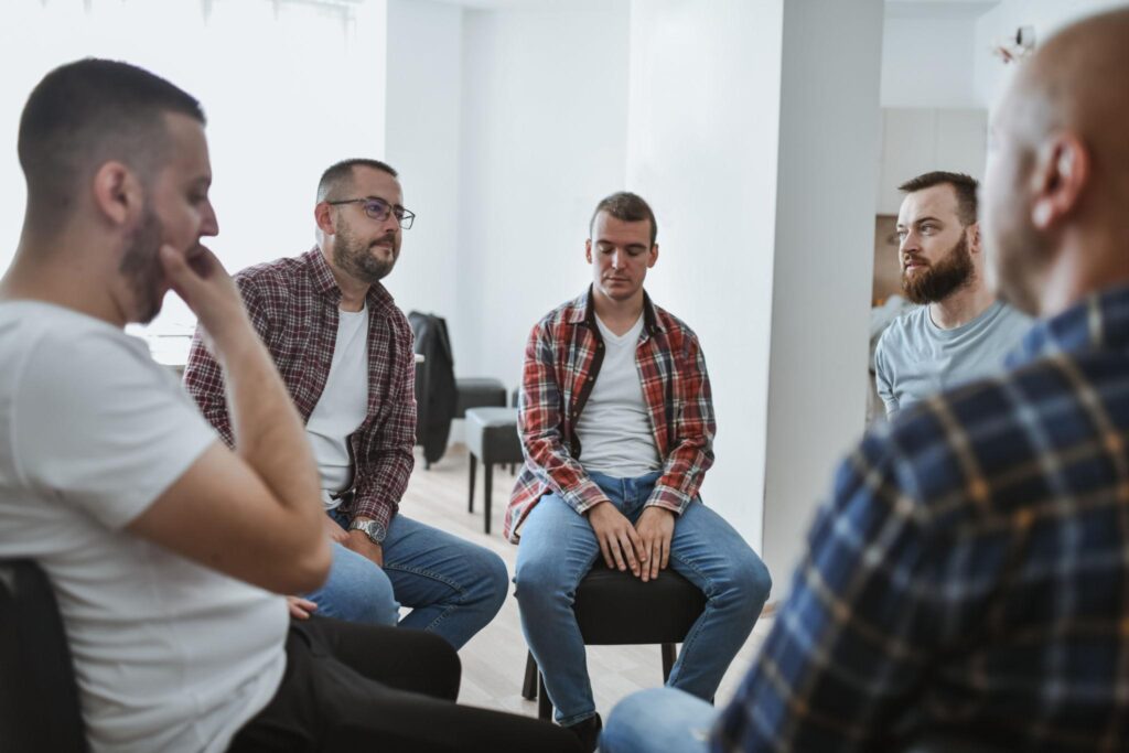 Alt text: Group of men sitting in a circle during therapy, offering peer support and open conversation for depression in men and mental health challenges