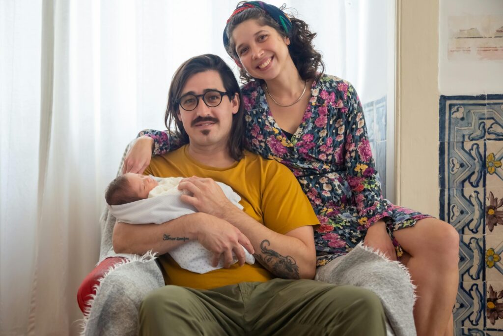 Father holding a newborn with partner beside him, representing family support and connection during postpartum adjustment and mental health in men
