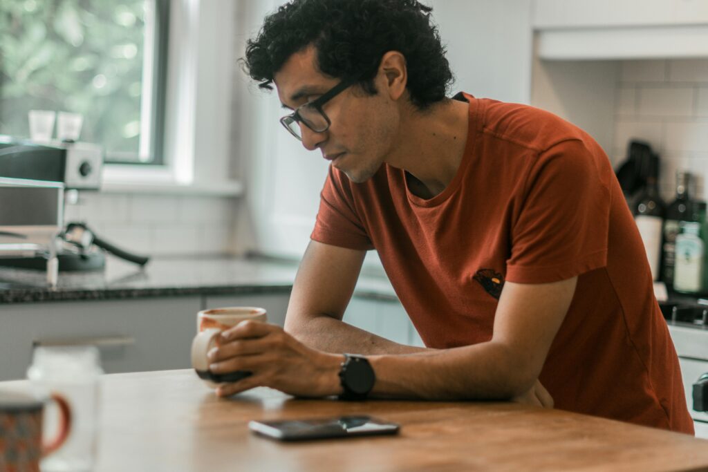 Man sitting alone at a kitchen table holding a coffee mug, showing signs of depression in men such as low energy, withdrawal, and quiet emotional strain
