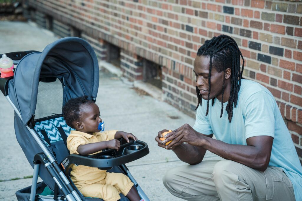 Father interacting with his baby in a stroller outdoors, showing everyday connection and caregiving while navigating mental health and parenting responsibilities
