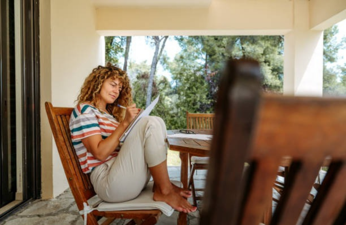 A woman sitting peacefully on a porch with a notebook