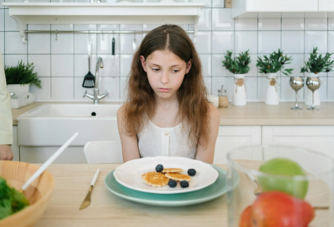 Child sitting quietly at a kitchen table before school, looking down at their breakfast with a subdued, thoughtful expression, reflecting feelings of back-to-school anxiety in a calm morning home setting.