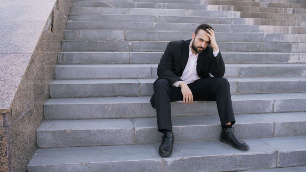 Business professional sitting on steps outside, appearing withdrawn ahead of a suicide prevention conversation
